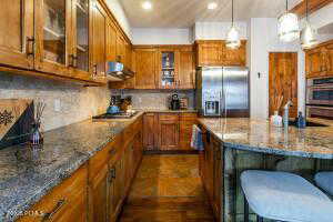 Kitchen featuring decorative light fixtures, backsplash, stone counters, a breakfast bar, and appliances with stainless steel finishes