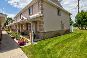 View of side of property featuring stucco siding, brick siding, a lawn, and a porch