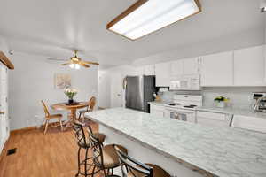 Kitchen with white appliances, visible vents, light wood-style floors, white cabinetry, and a sink