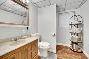 Bathroom with baseboards, toilet, wood finished floors, vanity, and a paneled ceiling