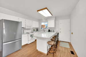 Kitchen featuring a breakfast bar area, light countertops, white cabinetry, white appliances, and a peninsula