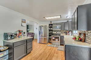 Kitchen with arched walkways, gray cabinetry, stainless steel appliances, a sink, and light countertops