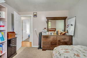 Bedroom with a textured ceiling, baseboards, and light colored carpet