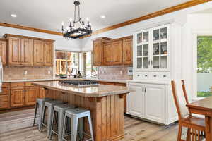 Kitchen featuring crown molding, a kitchen island, glass insert cabinets, and brown cabinets