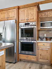 Kitchen with appliances with stainless steel finishes, light wood-type flooring, brown cabinets, and light countertops