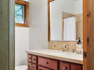 Bathroom with stone tile floors, curtained shower, backsplash, toilet, and vanity