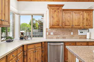 Kitchen featuring brown cabinets, tasteful backsplash, light countertops, stainless steel dishwasher, and a sink