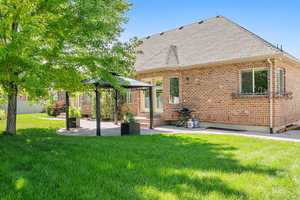 Rear view of house with a shingled roof, a lawn, a patio, a gazebo, and brick siding