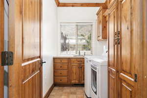 Laundry area featuring cabinet space, stone finish flooring, crown molding, separate washer and dryer, and a sink