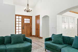 Living area featuring baseboards, arched walkways, an inviting chandelier, light wood-type flooring, and high vaulted ceiling