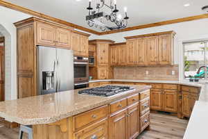 Kitchen with a breakfast bar, stainless steel appliances, hanging light fixtures, backsplash, and ornamental molding