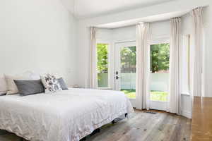 Bedroom with light wood-style floors, access to outside, multiple windows, and vaulted ceiling