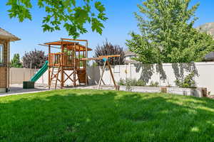 View of jungle gym with a garden, a yard, and a fenced backyard