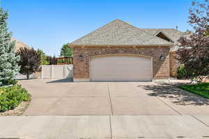 View of front facade with brick siding, driveway, an attached garage, and fence