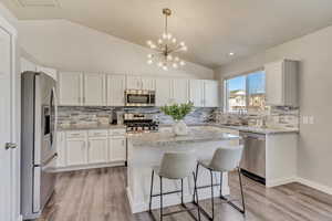 Kitchen with white cabinets, lofted ceiling, a center island, stainless steel appliances, and a sink