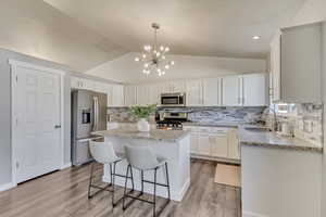 Kitchen with stainless steel appliances, a sink, white cabinetry, vaulted ceiling, and a center island