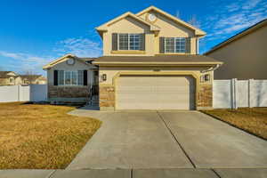 Traditional-style house featuring driveway, a garage, stone siding, fence, and stucco siding