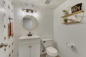 Half bath with toilet, visible vents, vanity, and baseboards