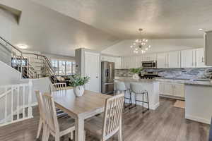 Dining area featuring stairs, a notable chandelier, vaulted ceiling, and wood finished floors