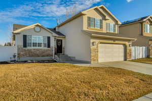 Traditional-style home featuring fence, stone siding, driveway, stucco siding, and a front lawn