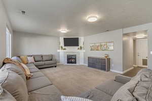 Living room featuring light carpet, a lit fireplace, visible vents, and baseboards