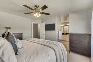 Bedroom with a textured ceiling, ceiling fan, light carpet, and ensuite bath