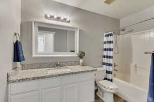 Bathroom featuring a textured ceiling, toilet, vanity, visible vents, and shower / bath combination with curtain