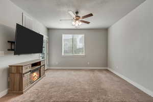 Unfurnished living room featuring light colored carpet, visible vents, a glass covered fireplace, ceiling fan, and baseboards