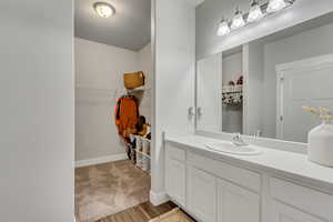 Bathroom featuring a textured ceiling, wood finished floors, vanity, baseboards, and a spacious closet