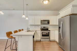 Kitchen featuring decorative light fixtures, stainless steel appliances, light countertops, a kitchen bar, and white cabinetry