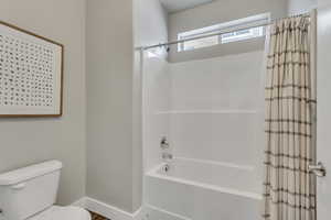 Bathroom with shower / tub combo, toilet, and baseboards