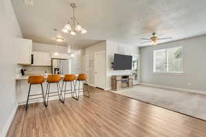 Kitchen with white cabinetry, open floor plan, light countertops, stainless steel fridge, and decorative light fixtures