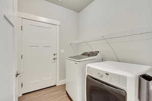 Clothes washing area with light wood-type flooring, laundry area, and washing machine and dryer