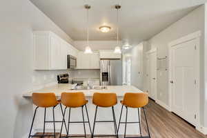 Kitchen featuring white cabinets, stainless steel appliances, light countertops, pendant lighting, and a sink