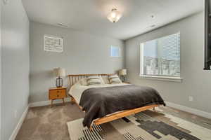 Bedroom with light carpet, multiple windows, and visible vents