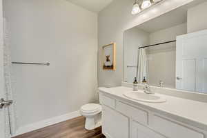 Bathroom with curtained shower, toilet, vanity, wood finished floors, and baseboards