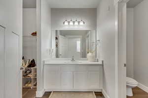 Bathroom with wood finished floors, a walk in closet, toilet, and baseboards