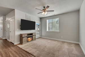 Unfurnished living room with a ceiling fan, a glass covered fireplace, visible vents, and baseboards