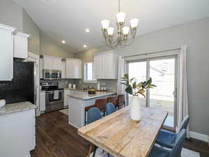 Kitchen with dark wood finished floors, lofted ceiling, hanging light fixtures, appliances with stainless steel finishes, and white cabinets