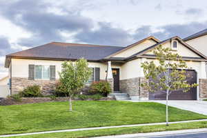 View of front of house featuring stone siding, driveway, an attached garage, and stucco siding