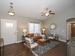 Living room with baseboards, arched walkways, dark wood finished floors, ceiling fan, and vaulted ceiling