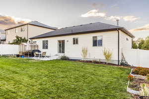 Back of property at dusk with a patio, a yard, roof with shingles, and a fenced backyard