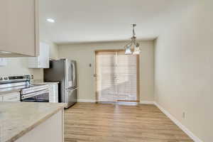 Kitchen featuring wood finish floors, hanging light fixtures, appliances with stainless steel finishes, white cabinets, and baseboards