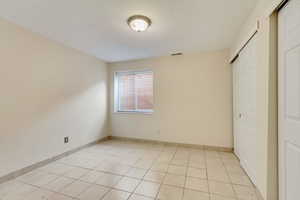 Unfurnished bedroom with a closet, light tile patterned flooring, visible vents, and baseboards