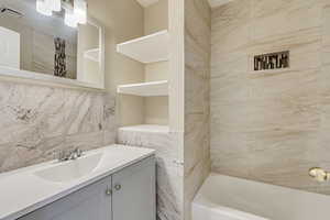 Full bathroom with shower / washtub combination, tile walls, tasteful backsplash, visible vents, and vanity