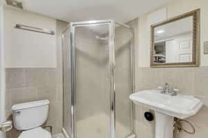 Bathroom with toilet, a stall shower, visible vents, and tile walls