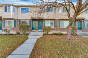 Townhome / multi-family property featuring entry steps, a front yard, and brick siding