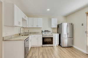 Kitchen featuring appliances with stainless steel finishes, wood tiled floor, white cabinetry, and a sink