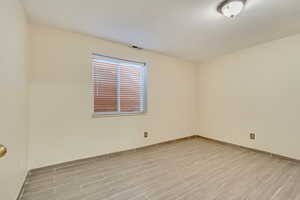 Empty room with wood tiled floor, visible vents, and baseboards