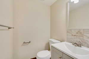 Half bathroom with toilet, vanity, and decorative backsplash